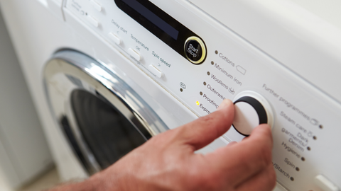 Man's hand adjusts the settings on a washing machine. | Heat Holders®