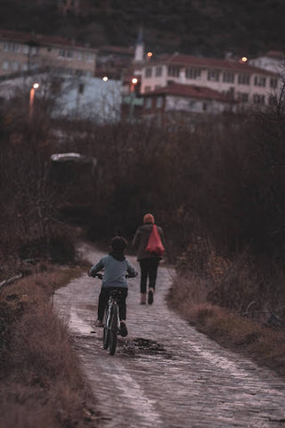 A child rides his bike on the road, following his mother who is walking.