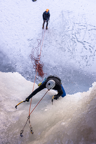 Man ice climbing while another man controls the rope at the bottom. | Heat Holders®