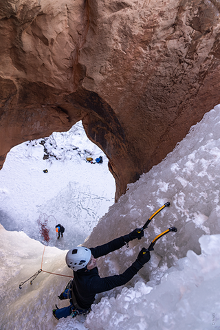 Man ice climbing up mountain while another man takes care of the rope at the bottom. | Heat Holders®