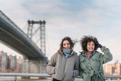 Two women stand in the wind with a bridge in the background. | Heat Holders® and Raynauds