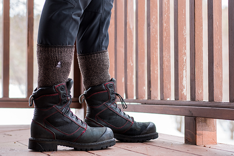Person stands on a porch in the winter. Keep your feet warm in wool socks. | Heat Holders®