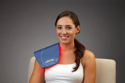 Smiling woman using Celluma red light therapy device on shoulder