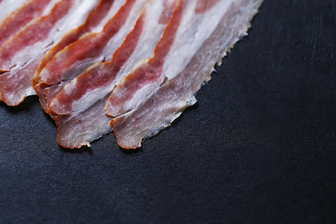 Raw bacon on a black stone plate.