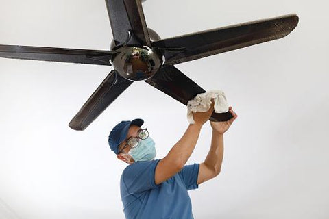 man wearing a protective mask cleaning ceiling fan