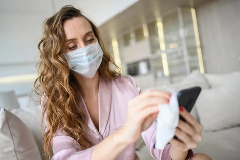 Mulher com máscara, limpando o celular com pano para limpar as bactérias.