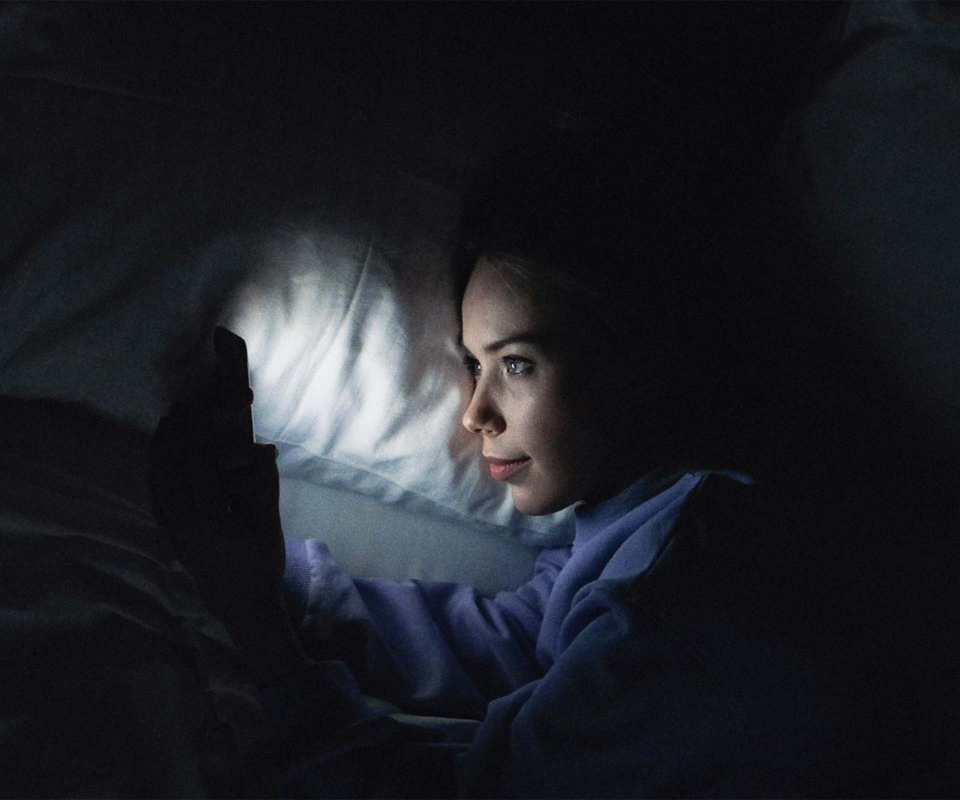 A woman in bed with her smartphone glowing in the night