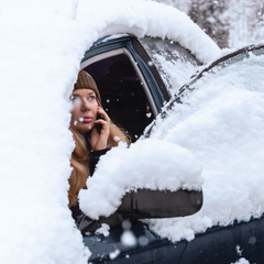 woman on a phone stuck in a snowy car with a dead battery
