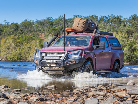 Red offroad truck camper crossing a stream of water