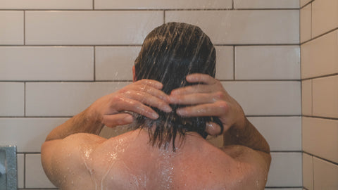 Man washing hair in shower, with white tile