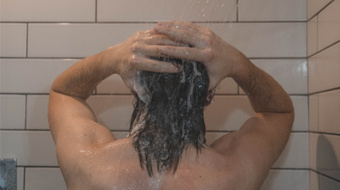 Man rinsing hair in shower, with white tile.