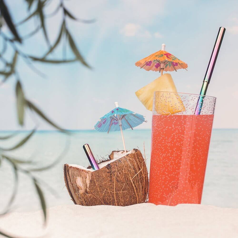 A glass of juice, a coconut, and two umbrellas on the beach