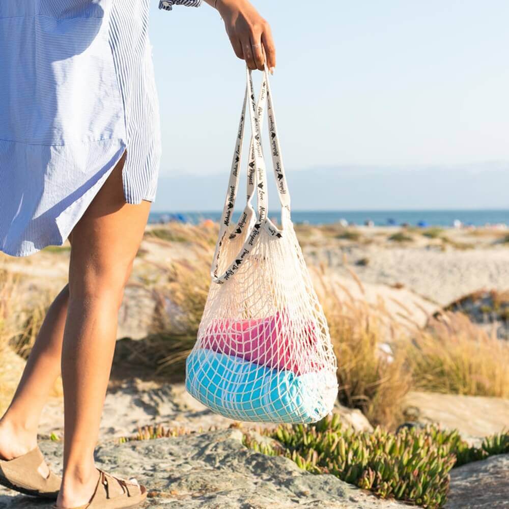 A woman enjoying time on the beach with Shaka Love eco-friendly bag on hand