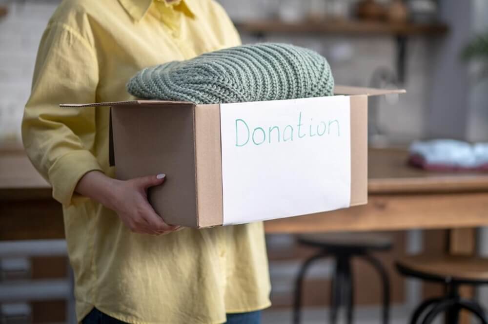 cropped photo female volunteer holding a carton full clothes prepared for donation