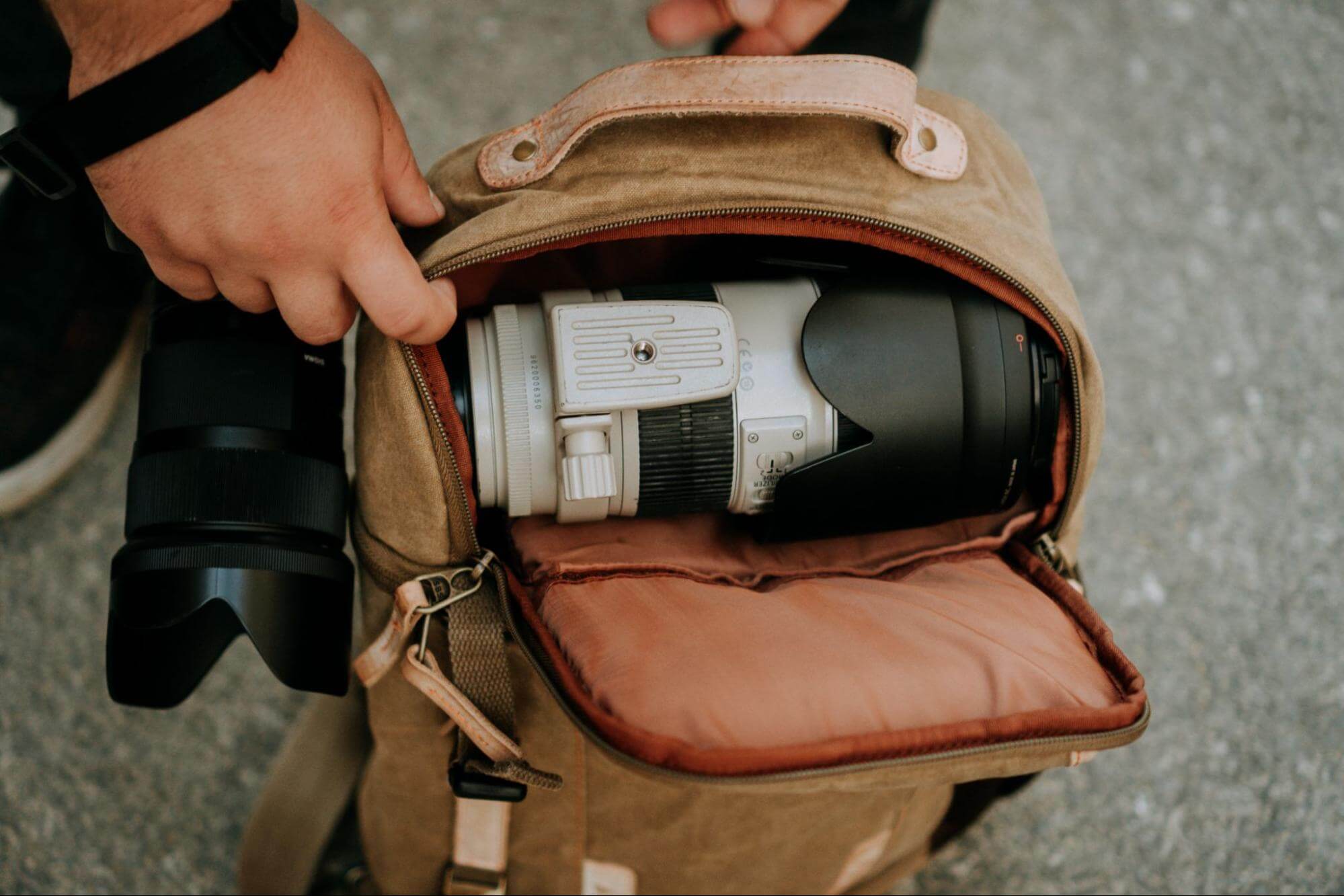 Traveler taking out white camera lens from his backpack to maximize every square inch of storage