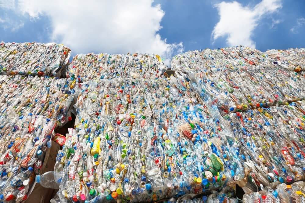 Close-up view of a recycling center, showcasing a towering pile of colorful plastic bottles against a clear blue sky with mountains on the horizon