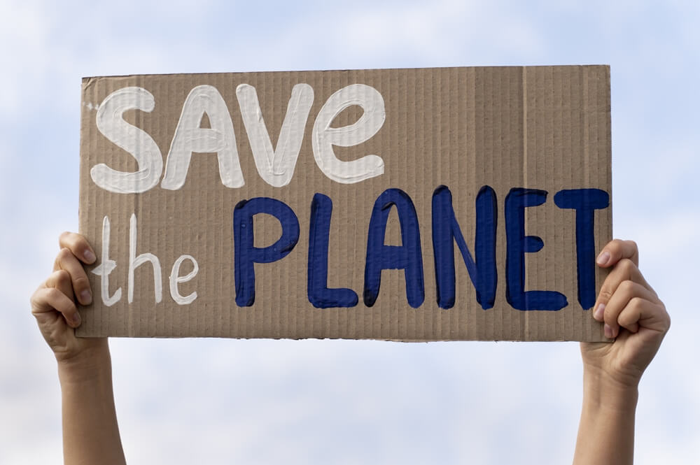 A person holding a cardboard sign that reads "save the planet" in protest against climate change