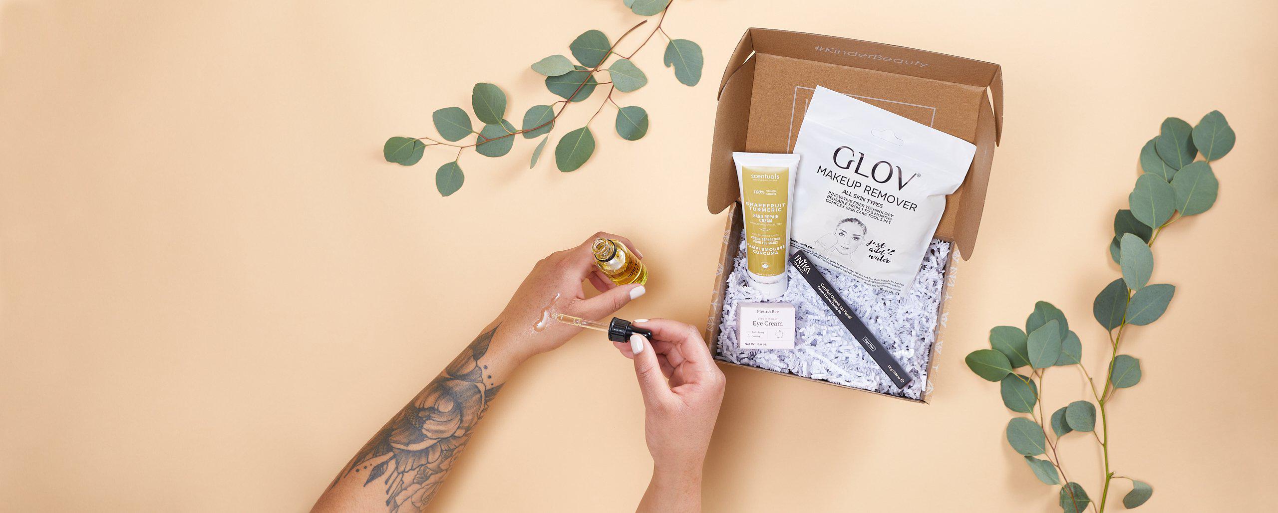 Image of two hands (one tattooed) opening a Kinder Beauty box with lots of clean, vegan, cruelty-free beauty products in the box.