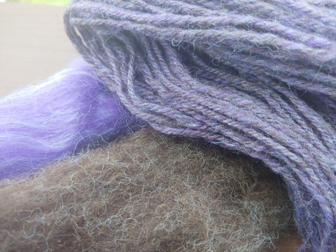 Dark Coopworth fiber and Violet 80/20 Merino/Tussah Fiber with yarn spun from blending the two lying on top.