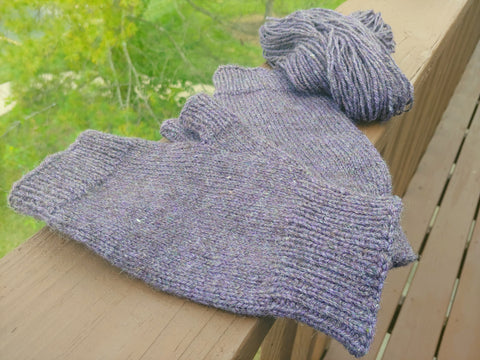A pair of fingerless mittens knit from a blend of Dark Coopworth and 80/20 Merino/Tussah lie on a painted wooden rail with some of the handspun yarn behind them.