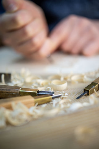 Cutting tools lie among wood shavings while the carver works.