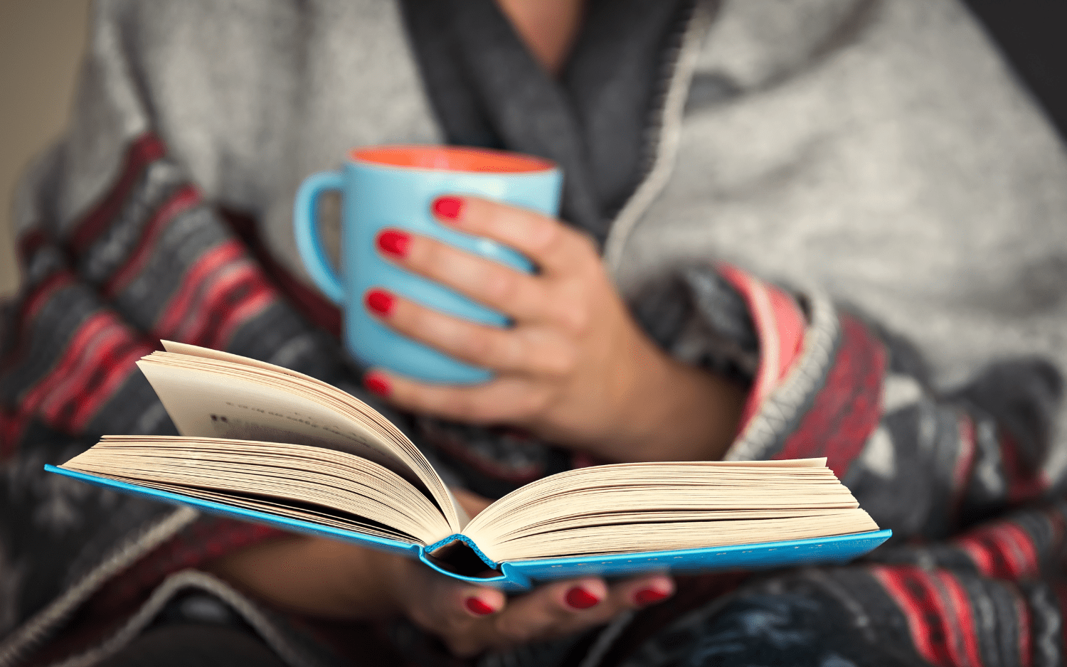 women reading cozily while drinking out of a mug 