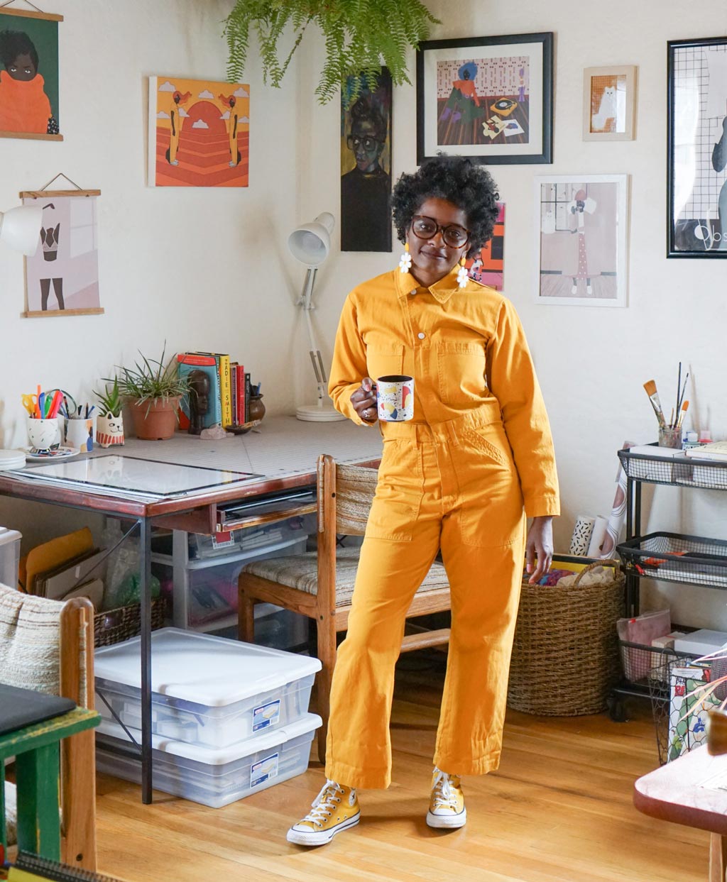 Janell Langford, standing in her art studio in a bold yellow jumpsuit