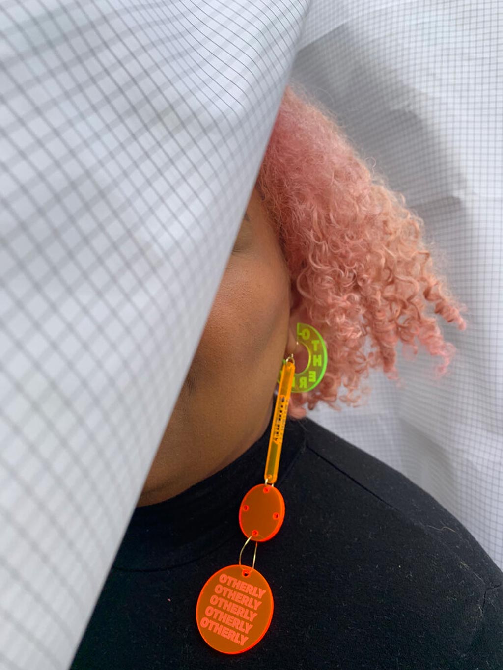 a close up of a brightly colored earring made of acyrlic. shown on the ear of a person with pastel pink hair