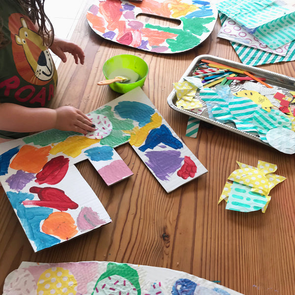 Child adding collage materials to large letters