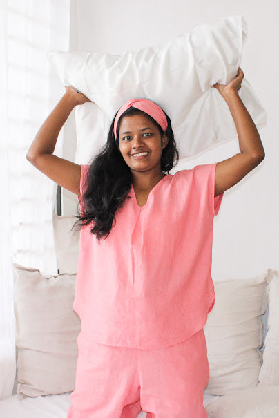 Model wearing Coral Pink Rest Collection holding the Peace Silk Pillowcase above her head. 