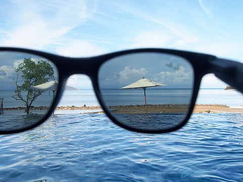 El mar y una pequeña playa mostrada a través de unos anteojos de sol polarizados de color negro con lentes grises. Se muestra el efecto del polarizado sobre los destellos de luz del agua. Los minimiza.