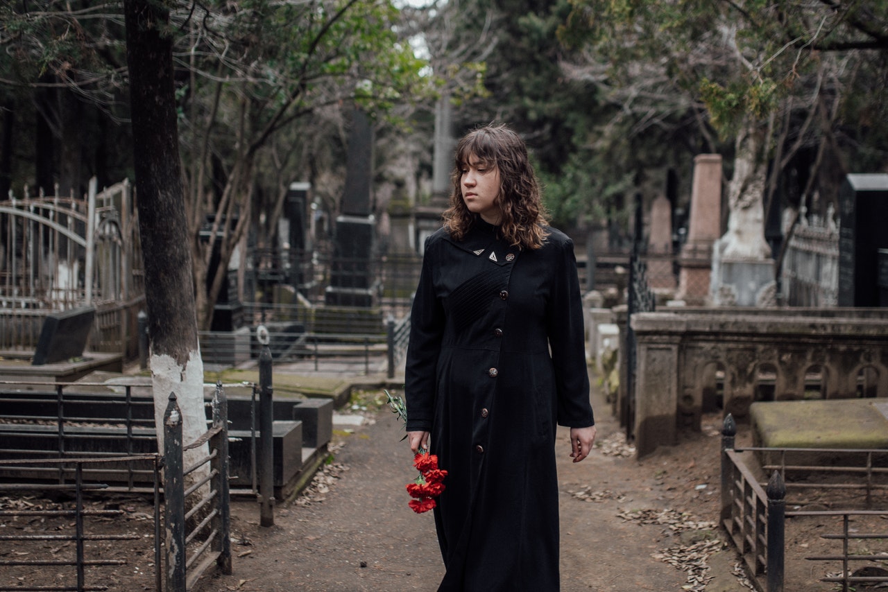 Femme marchant dans les allées d'un cimetiere avec un bouquet de rose