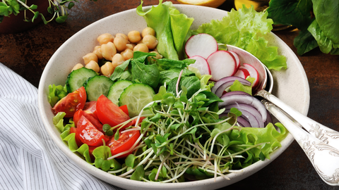 a large bowl of salad with a variety of vegetables, microgreens, and toppings