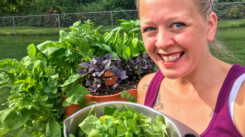 a woman posing in front of her Garden T 2 with a bowl of harvested herbs and greens