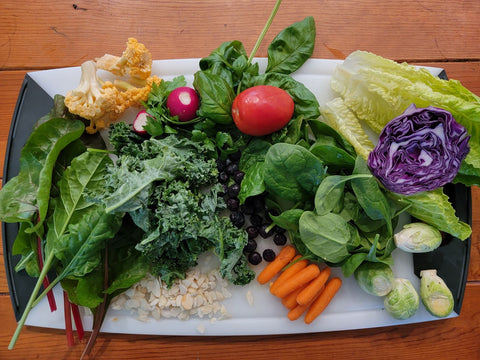 cauliflower, chard, kale, almond slivers, spinach, radishes, tomatoes, carrots, brussels sprouts, and purple cabbage cut and ready on a serving platter