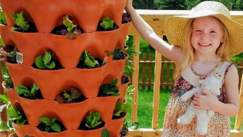 child holding a stuffed animal standing next to a vertical vegetable garden