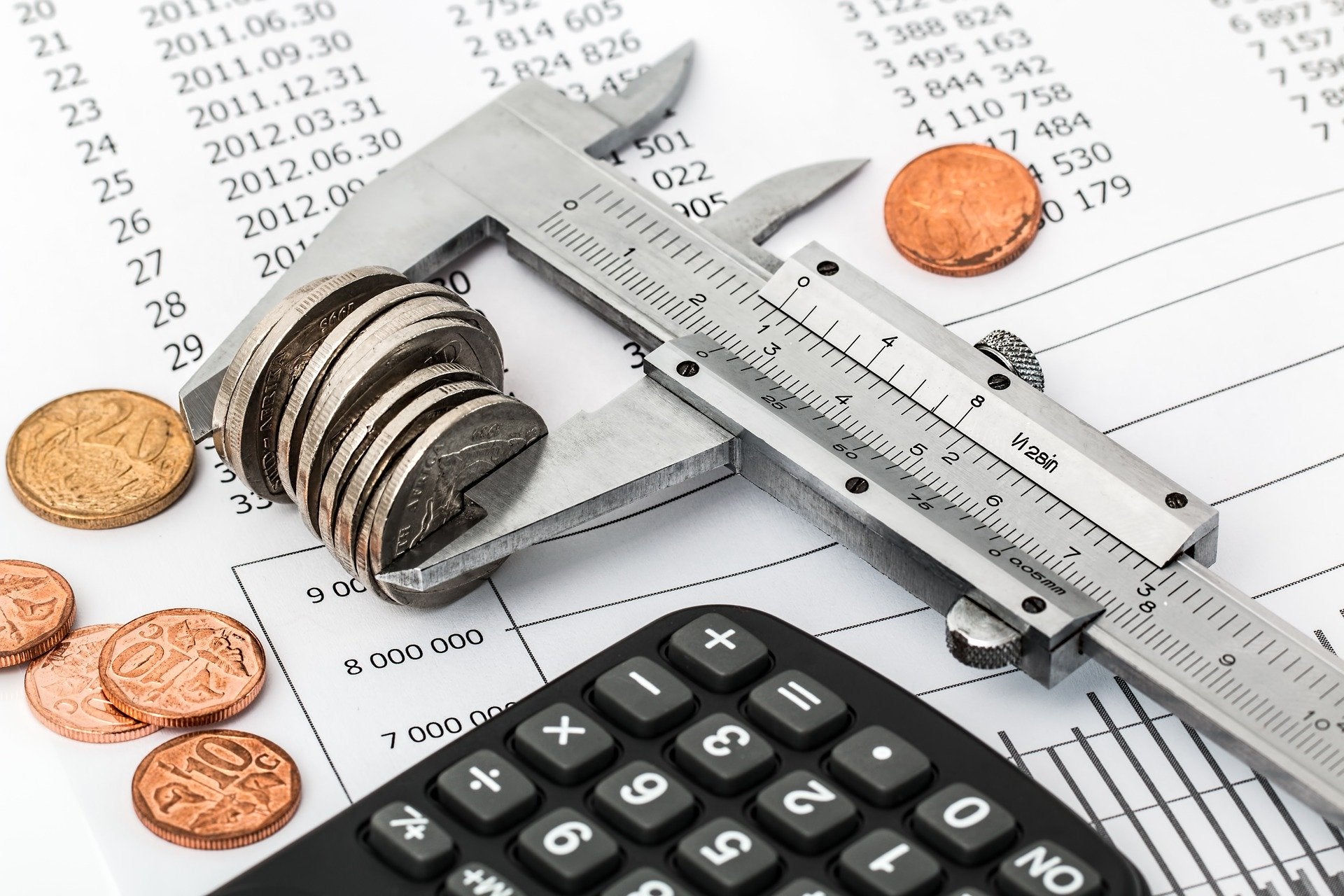  A caliper measuring a stack of coins sits on top of a calculator and financial documents, illustrating the concept of tracking and managing expenses during vacations.