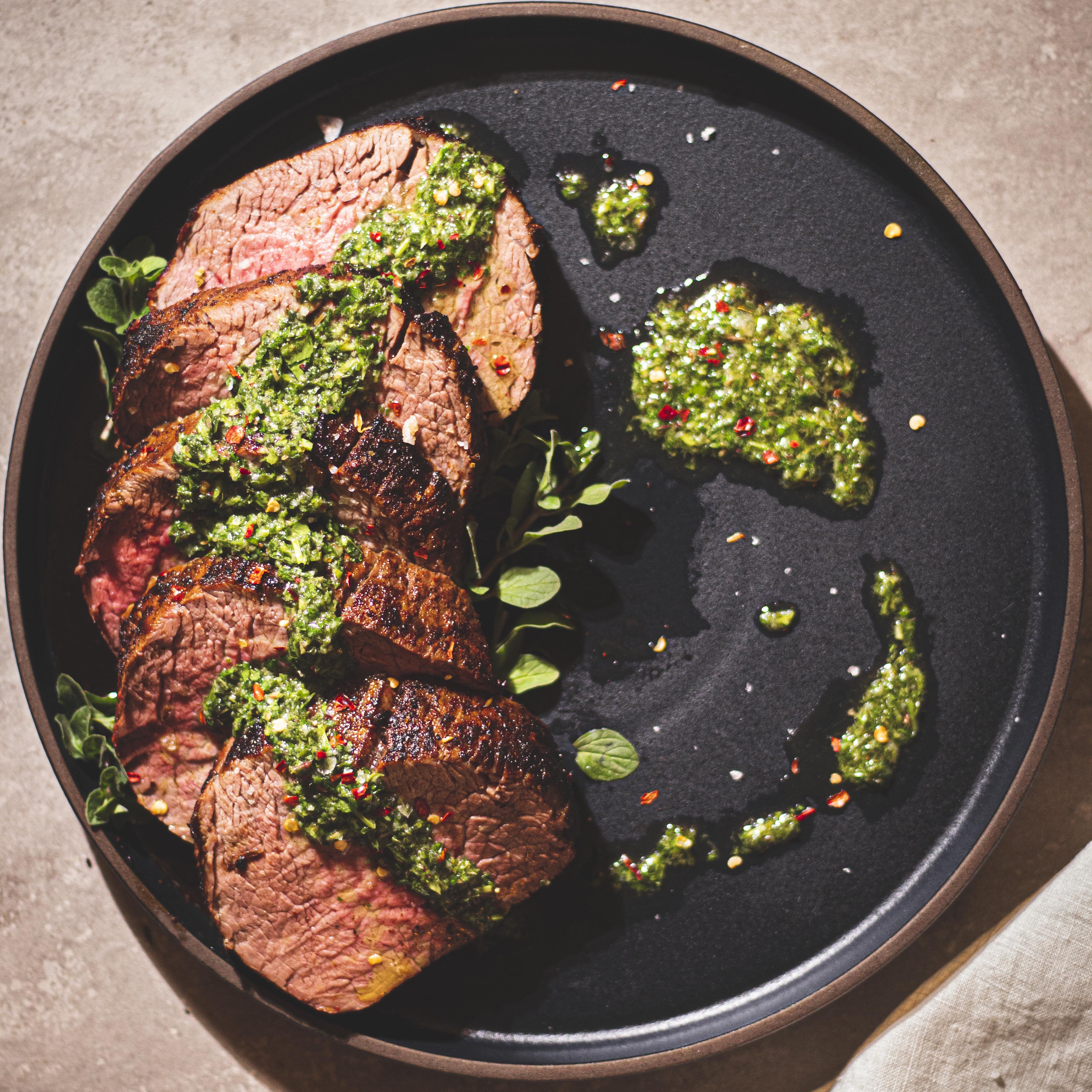Beef tenderloin in a skillet with chimichurri sauce