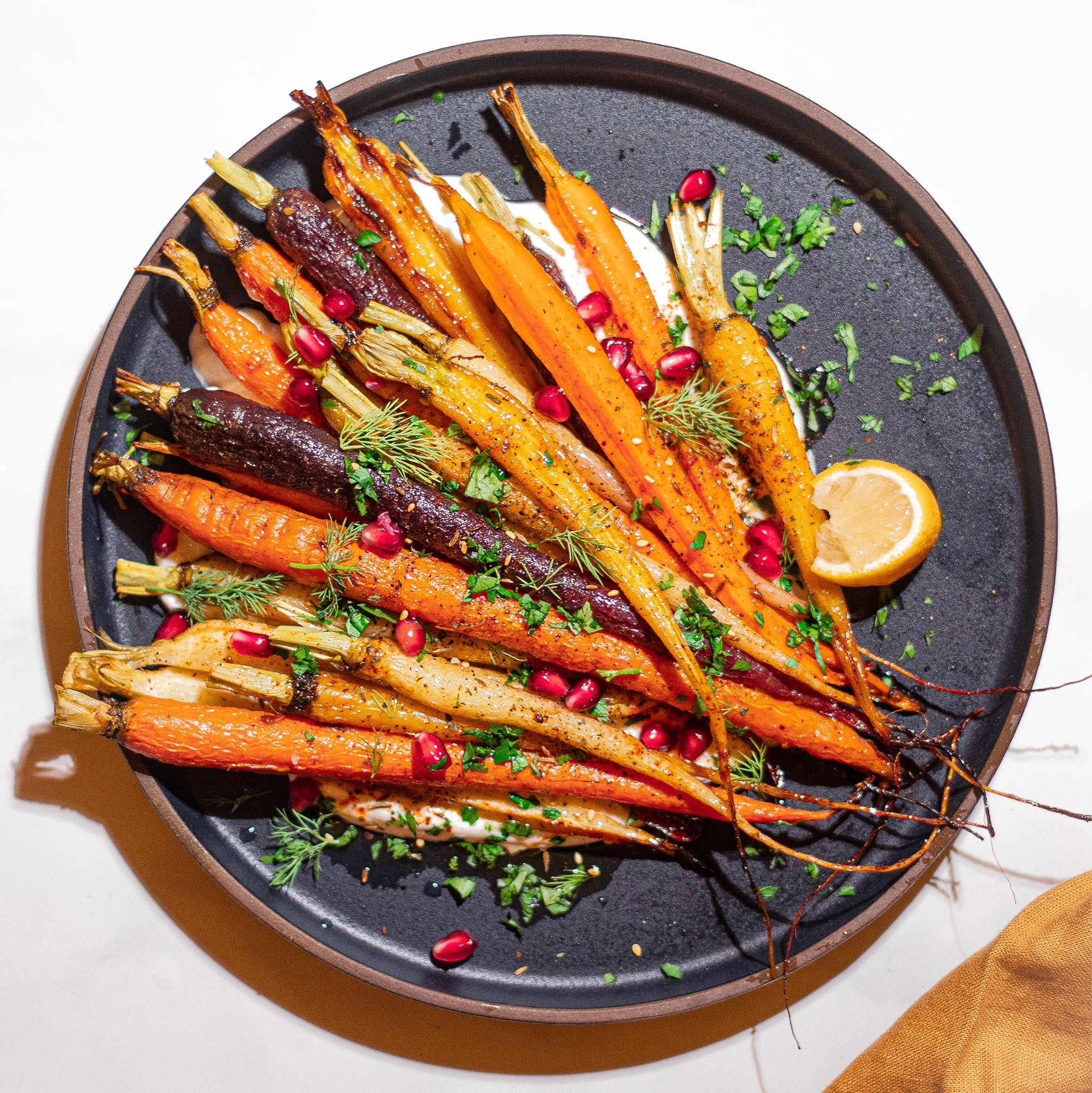 multi-colored carrots on black plate with pomegranate and honey