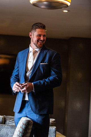 Groom stands getting ready in suit and tie