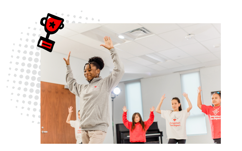 Four girls wearing red and white Jumpstart branded tshirts learning to dance from their coach who is wearing a grey sweatshirt.