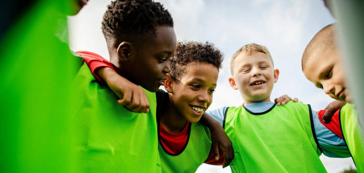 A group of four kids wearing athletic jerseys huddle together.