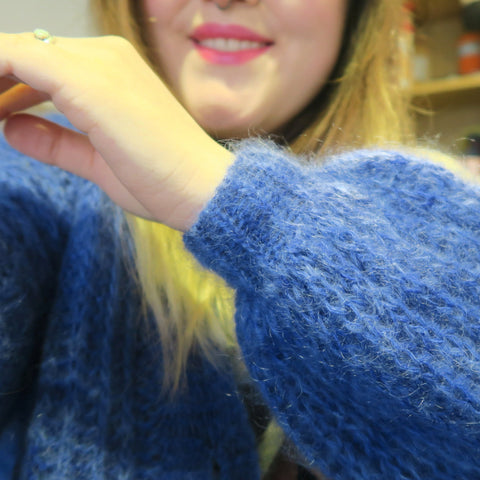 A white hand is in front of the camera, showing off a poofy sleeve with a tighter cuff, knit out of a fluffy, bright blue yarn.