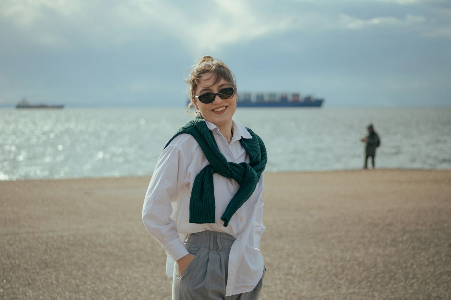 Woman wearing white shirt, green sweater, and sunglasses at the beach