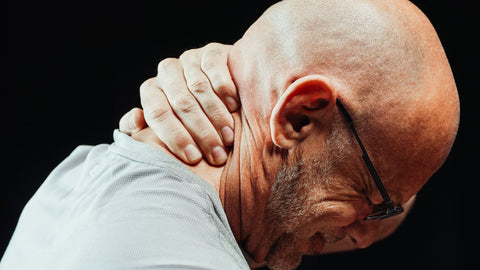 Bald man with glasses and beard winces with neck pain as his hand is on his neck
