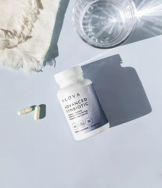 A bottle of supplements with capsules, a glass of water, and a white fabric on a flat surface.