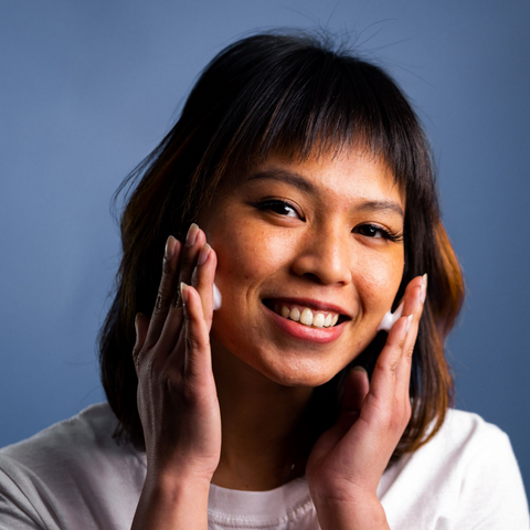 model applying facial wash to her face smiling