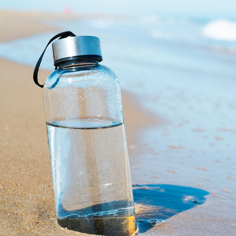 reusable glass water bottle in the sand on the beach 