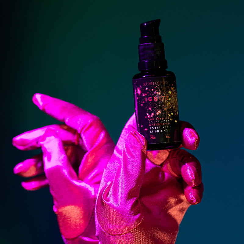 Red silk gloves holding a bottle of Kush Queen Personal Lube.