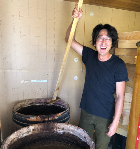 Osamu Uchida smiles with a tank of soy sauce 